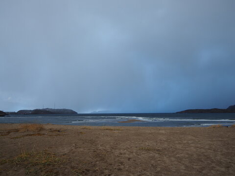 Gloomy day at the coast with dark stormy clouds over a sandy beach and calm sea