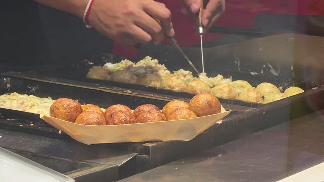 chef cooking delicious Japanese takoyaki octopus balls on hot griddle pan at street food stall market
