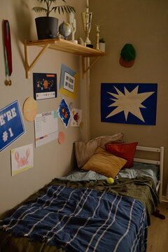 Vertical shot of teenager bedroom interior with bed and study schedule posters. Empty room setup suitable for youth lifestyle advertising and parenting editorial content