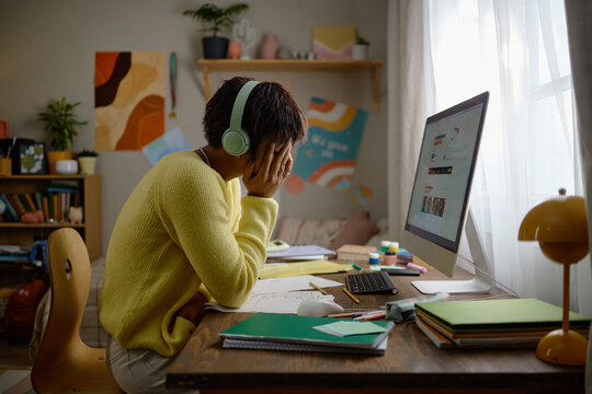 Tired teenager wearing headphones feeling stressed while studying online via desktop computer. Suitable for mental health awareness and remote education marketing