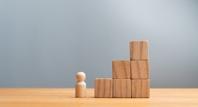 Wooden figure standing in front of wooden block staircases representing career growth, success, and business goal achievement
