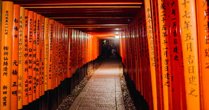 Kyoto, Japan - 12 April 2025: View of the iconic vermilion torii gates at Fushimi Inari Taisha, featuring rows of wooden pillars with black bases and traditional Japanese calligraphy.