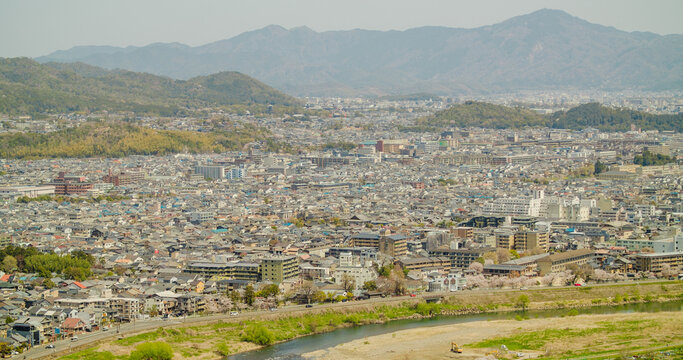 Kyoto, Japan - 10 April 2025: View of Arashiyama district featuring the Katsura River, dense urban architecture, and surrounding mountains under a clear sky.