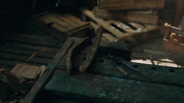 Amidst shadows and splintered wood, aged tools lie quietly on a worn surface. Dust dances in the faint light, revealing a hidden world of craftsmanship and history.