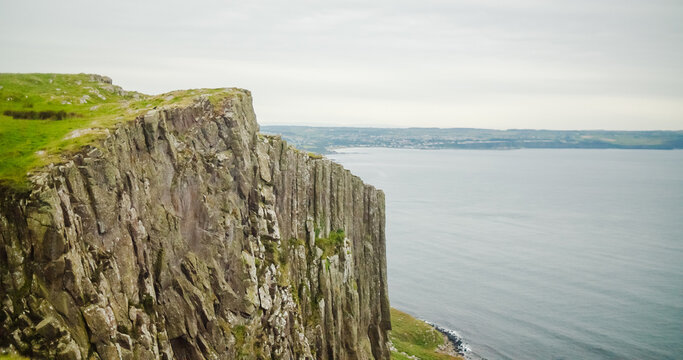 Ballycastle, United Kingdom - 14 September 2024: View of Fair Head, a dramatic cliff face rising above the sea with lush green grass on top under an overcast sky.