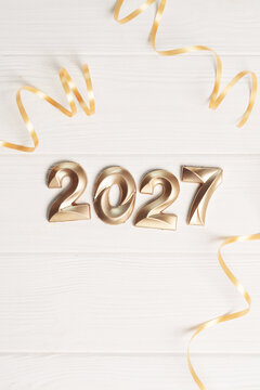 Vertical new year 2027 card background with golden numbers and swirling ribbons on white wood with copy space below