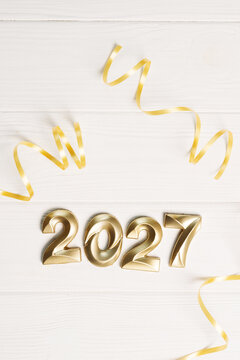Gold 2027 figures with curly party ribbons on white boards, vertical holiday background for calendar and invitation