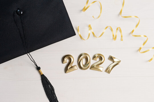 Class of 2027 concept with black graduation cap in the corner and small golden numbers on white wood
