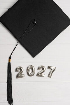 Vertical graduation 2027 background with black mortarboard, long tassel and silver numbers on white planks