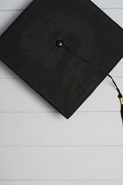 Vertical close up of black graduation cap with tassel on white wooden background with empty space for text