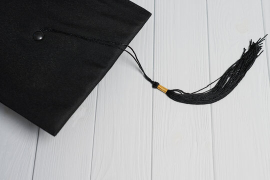 Graduation cap in the corner with long tassel stretched across light gray wooden planks, copy space