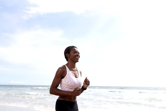 Person jogging on a beach, wearing athletic gear, under a clear sky.