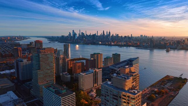 Jersey City buildings face the Midtown Manhattan skyline. The Hudson River separates glass waterfront towers from distant skyscrapers beneath streaked clouds.