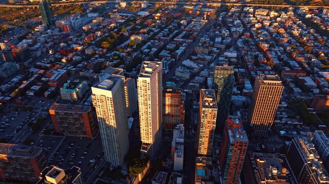 Apartment towers rise above the Jersey City street grid. Sunlit facades and rooftop equipment contrast with dark blocks of low buildings viewed from above.