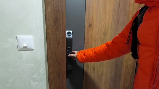 Male hand typing passcode on electronic lock of wooden door, entering apartment as it opens. Illustrates keyless apartment entry, automated home security technology, and modern rental access.