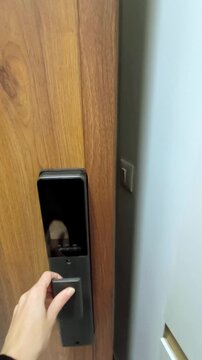 Woman&rsquo;s hand presses release button on electronic lock built into wooden door, then pulls handle to open it. Symbolizes leaving modern apartment, keyless convenience, and smart home technology.