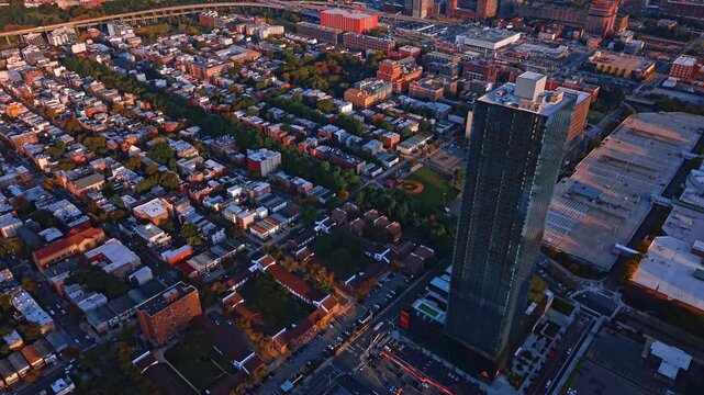 A tall apartment tower overlooks streets and houses in Jersey City. A dark rectangular facade rises at the right above rows of flat roofs and intersecting roads.