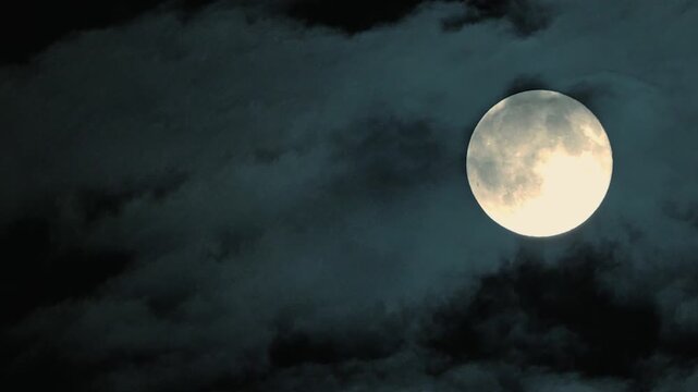 Night sky with full moon glowing behind dark clouds, lunar surface details visible. Clouds drift across moonlit sky, creating dramatic contrast. Lunar surface craters and maria clearly visible