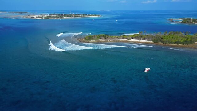 High angle drone shot of safari boat anchored in clear turquoise ocean near coral reef island break with surfing waves. Great stock asset for travel and sports edits.Himmafushi.Maldives