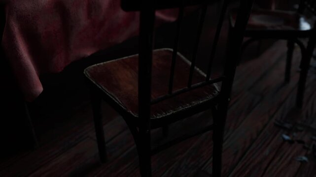 Empty wooden chairs placed near a table covered with a pink cloth inside a room during the late evening hours. Shadows fall across the dark floorboards as soft light touches the furniture surfaces.