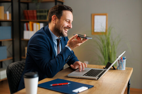 Businessman speaking into smartphone while working on laptop