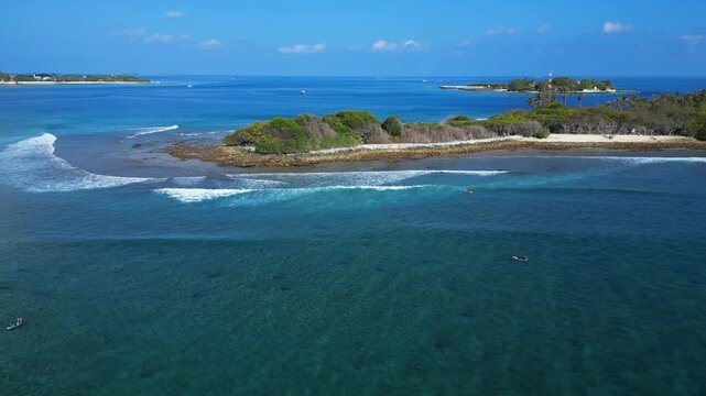 High angle aerial drone shot of surfers paddling in clear blue ocean water near tropical island reef and surf waves. Great background for travel and sports edits. Maldives