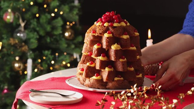 Hands gently rotate a festive Italian pandoro cake filled with pastry cream and fresh raspberries and red currants. Christmas dinner table.