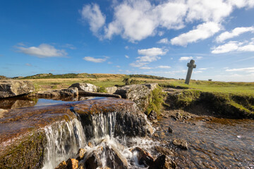 Rocky stream cascades beneath a weathered stone cross in open grassland © worldimage
