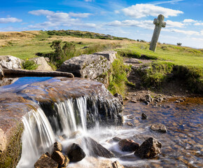 Rocky stream cascades beneath a weathered stone cross in open grassland © worldimage