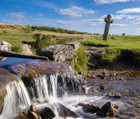 Rocky stream cascades beneath a weathered stone cross in open grassland © worldimage