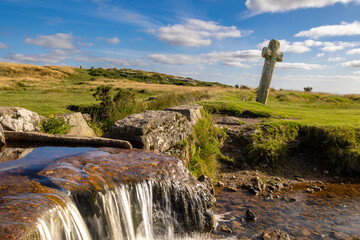 Rocky stream cascades beneath a weathered stone cross in open grassland © worldimage