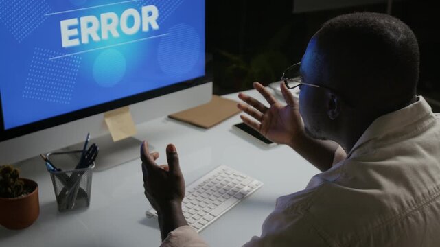 African American young adult man gesturing frustratedly at computer error screen. Clip ideal for IT support, software glitch, cyber security, data recovery, and workplace stress commercials