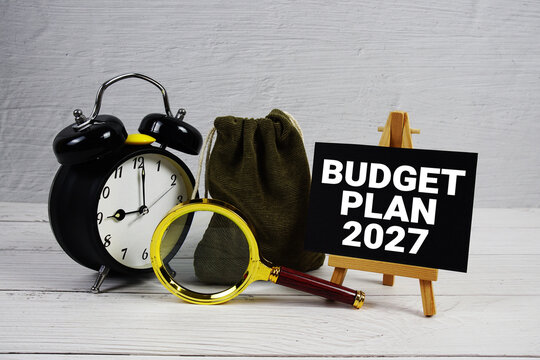 Budget Plan 2027 text with alarm clock and magnifying glass on wooden background