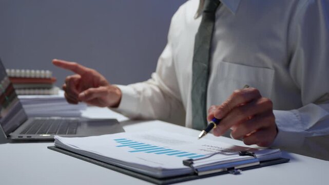 Professional accountant examining statistical reports with pen, working late hours on computer at office desk