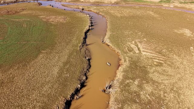 Aerial view follows a dried up river channel through exposed lakebed in France during the day