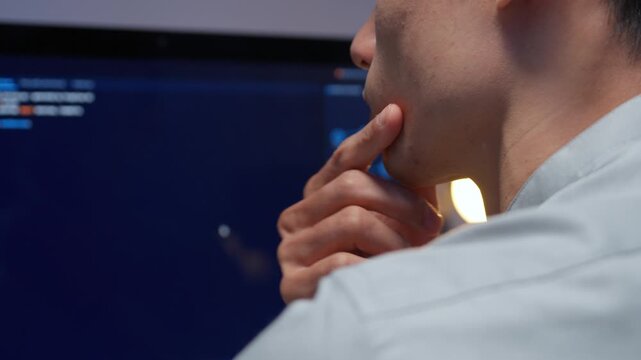 Asian software engineer thinking deeply while analyzing source code on computer screen in modern tech office