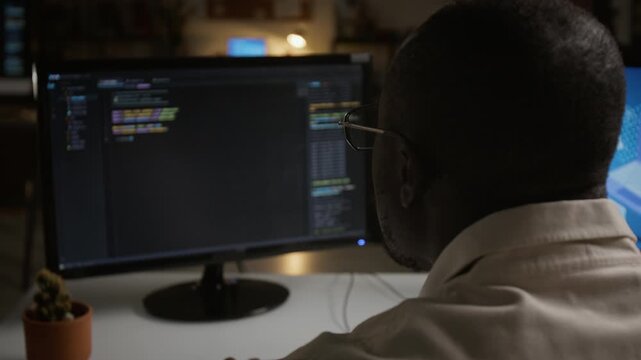Young adult African American software engineer writing code on computer monitor in office, over the shoulder shot. Perfect for technology advertising, IT campaigns, coding tutorials