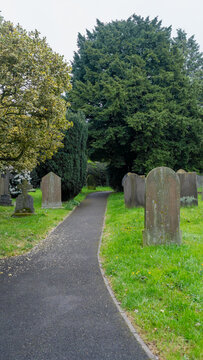 A wide paved path running through an old church cemetery, surrounded by tall green trees