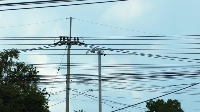 Messy electrical cables and security cameras on utility poles against bright blue sky