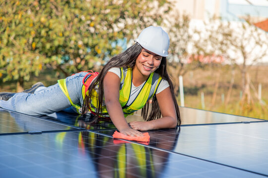 Female engineer cleaning solar panel, ensuring renewable energy system maintenance