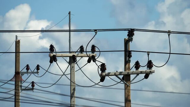 Messy electrical cables on concrete utility poles against cloudy sky in bright daylight