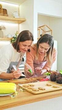 Two women decorate cookies together at a bright kitchen counter