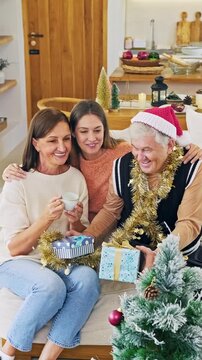 Three generations of women smile together while sharing Christmas gifts at home
