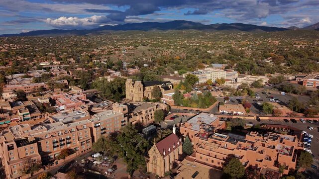 San Loretto chapel in Santa Fe, capital of New Mexico, USA. Aerial view of the Gothic church spire, adobe hotels and Cathedral Basilica, dark clouds over autumn hills and Sangre de Cristo Mountains.