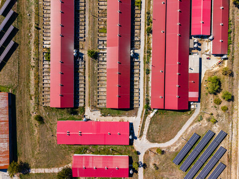 Aerial view of red-roofed farm buildings and solar panels beside railway tracks in daylight