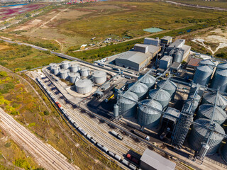 Rail lines and storage silos serving an industrial processing plant in a wide rural area during daylight © DSMT
