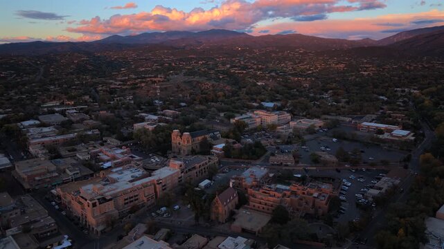 Dusk over Santa Fe, capital of New Mexico, USA. Aerial of Cathedral Basilica and Loretto Chapel among adobe hotels and parking lots. Pink clouds glow above the dark Sangre de Cristo Mountains.