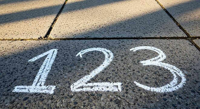A close-up view of the numbers 1 2 3 chalk drawn on grey outdoor concrete paving tiles representing early education concepts and basic counting skills.