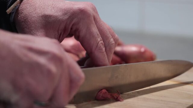 Stockholm, Sweden A cook cuts and peels shallots or onions on a wooden board with a large knife. 