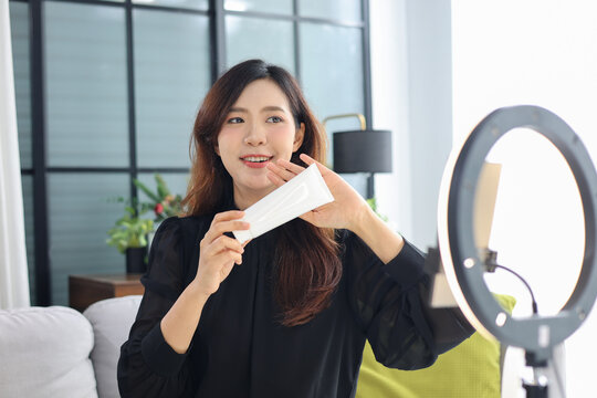 Asian woman filming beauty vlog tutorial with ring light, reviewing cosmetics cream moisturizer or lotion.